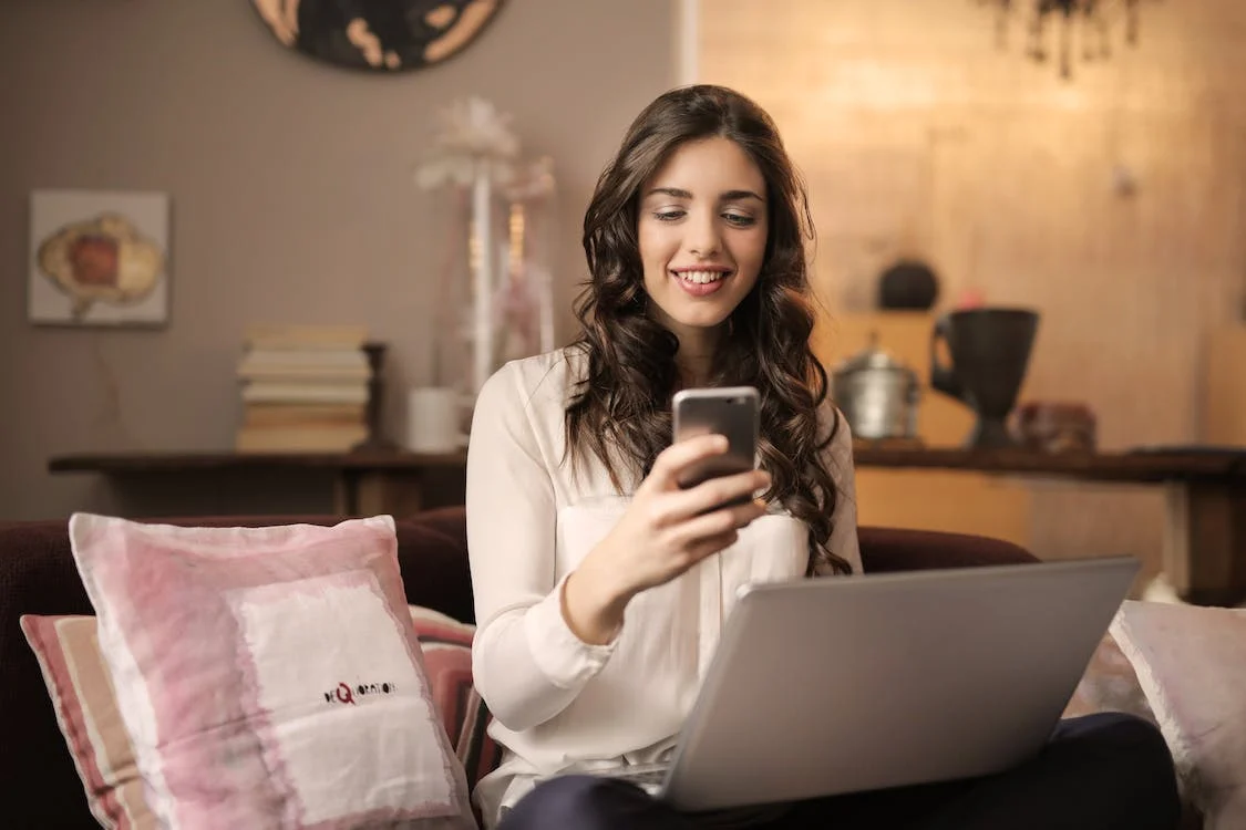 female using laptop and mobile, smiling