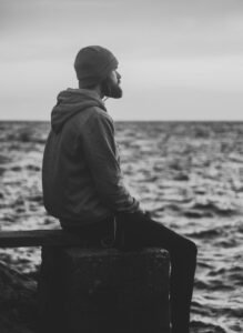 male sitting on a peer looking out to sea